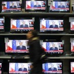 A woman walks past television screens showing Silvio Berlusconi's farewell speech: The controversial Italian politician may have resigned as prime minister, but he still controls much of the media.